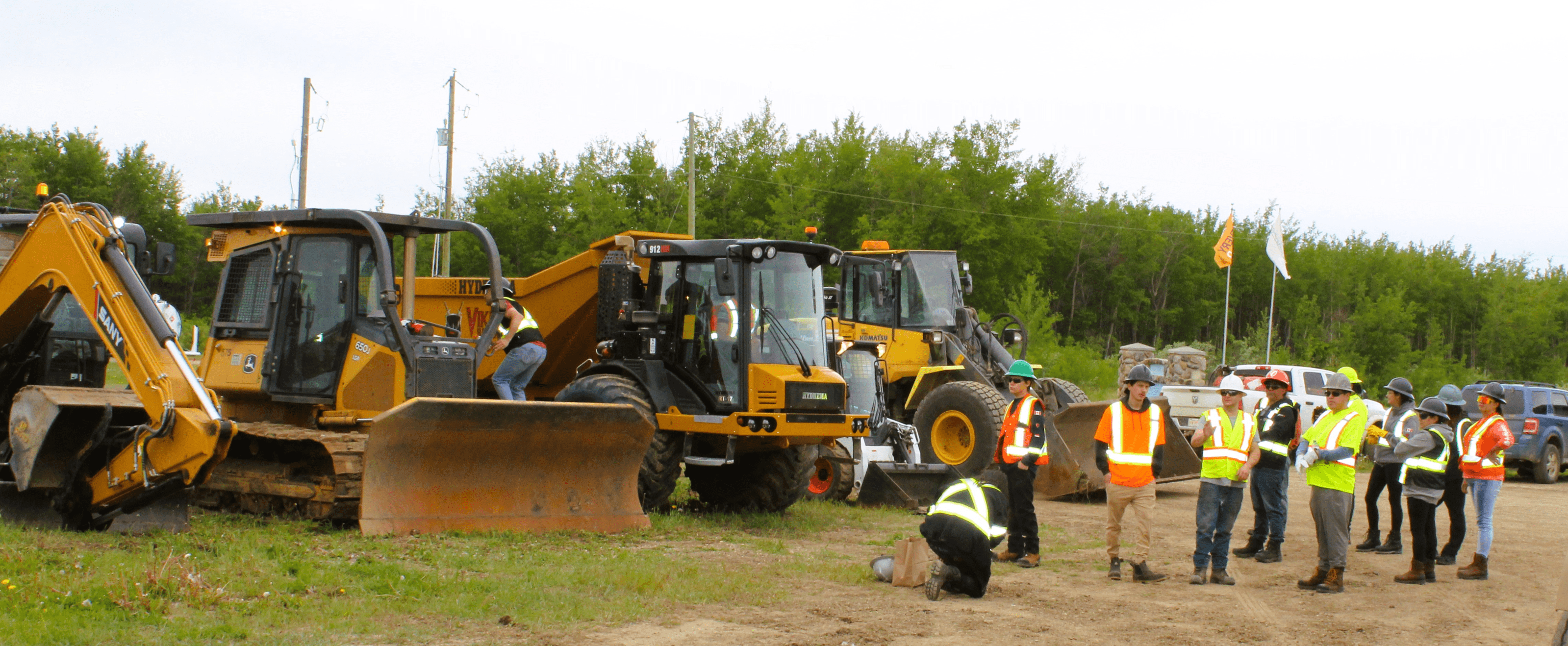 Construction workers operating heavy machinery on a site with greenery in the background.